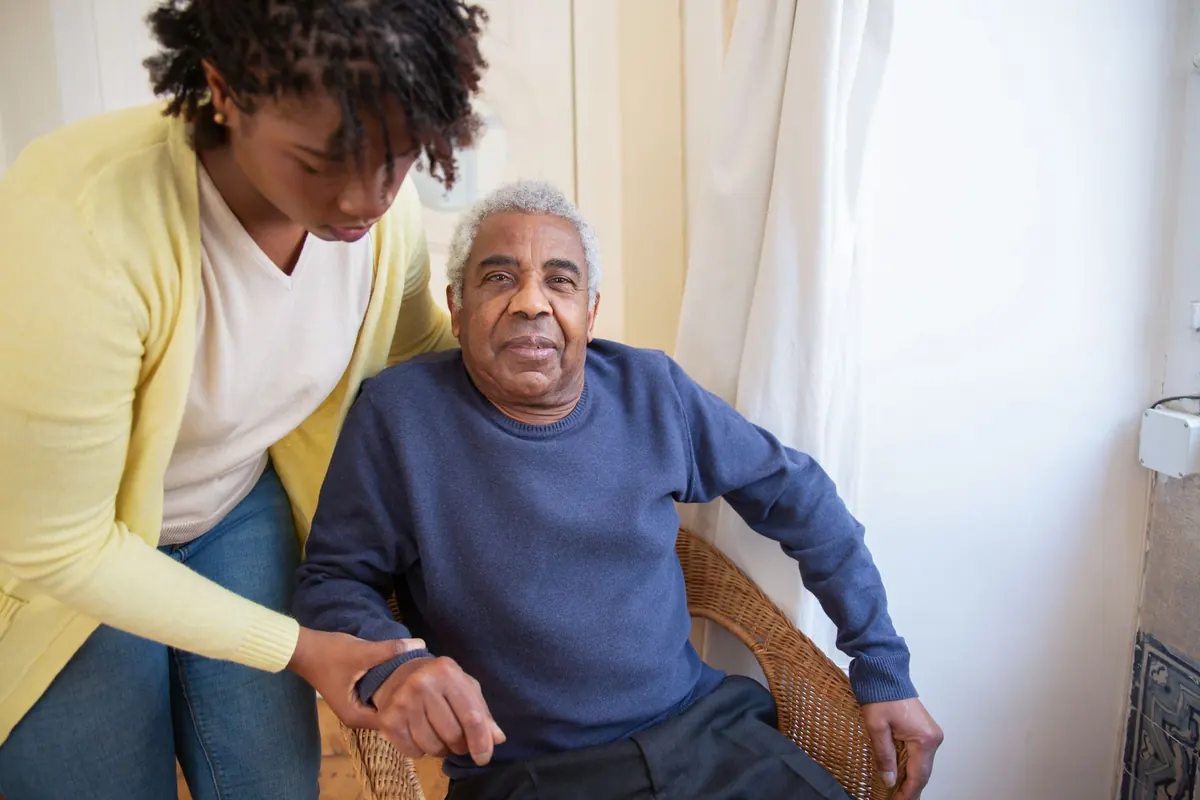 A carer sitting beside an older man in his chair at home