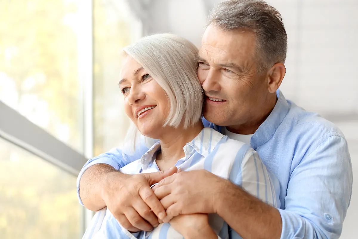 An older couple embracing by a bright window at home